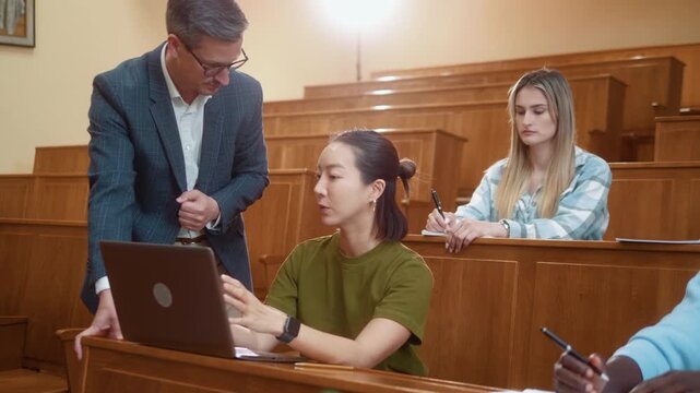 Professor communicating with Korean female student during university class. Educational discussion, mentoring and positive academic interaction in modern classroom.