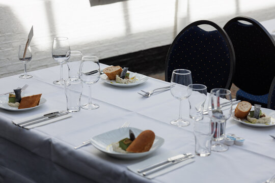 Elegant restaurant table setting with white linen, plates, cutlery and wine glasses in bright natural sunlight. Indoor fine dining scene showcasing luxury hospitality atmosphere