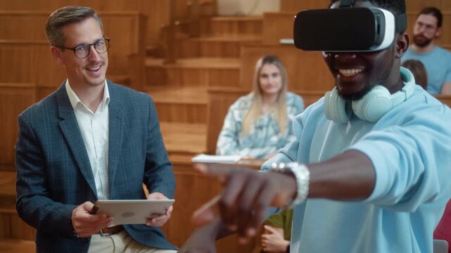 Professor with digital tablet guiding African student using VR headset during university class. Diverse students observe immersive learning experience with laptop and modern education technology.