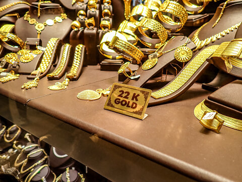 Close up of 22 karat gold jewelry including bracelets, necklaces and rings arranged on a shop counter with a sign indicating gold purity.