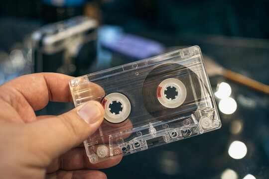 Vintage audio closeup of transparent cassette tape in hand, focused on physical media, collectible format, sound archive, nostalgia and analog music heritage.