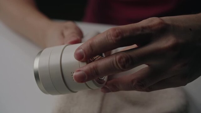 Hand holding electric lint remover, showing rotating blades starting up and spinning fast, demonstrating powerful fabric shaving and pilling removal machine, closeup. Shooting in slow motion.