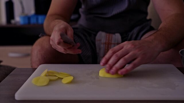 Close-up view of a man's hands expertly peeling and then precisely cutting raw potatoes on a kitchen cutting board. Ideal for illustrating food preparation, healthy eating, or culinary content.