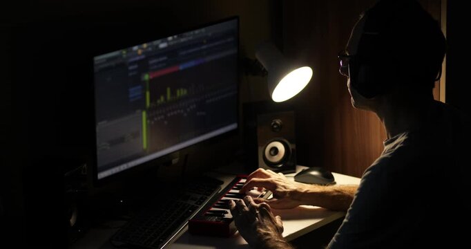 Music producer working in home studio at night, creating beats using keyboard and computer software. Independent artist producing music in bedroom studio. Home recording, digital production creative