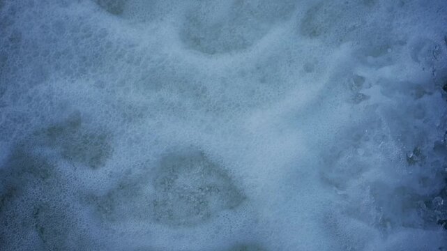 Fast flowing river drops over weir creating foamy waterfall with strong aeration recorded in slow motion detailed shot