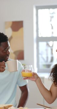 Vertical video: African American couple at home, woman offering juice, he clinking mug then sipping
