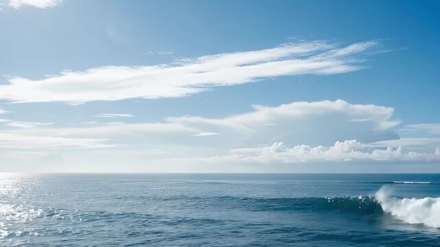 Vast ocean landscape with horizon line and breaking wave under a clear blue sky with white clouds