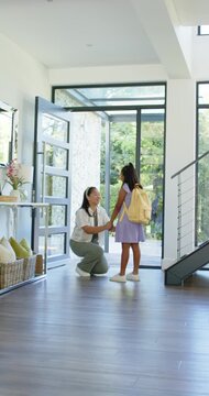 Vertical video: African American mom fixing yellow pack at door kissing girl leading out to school