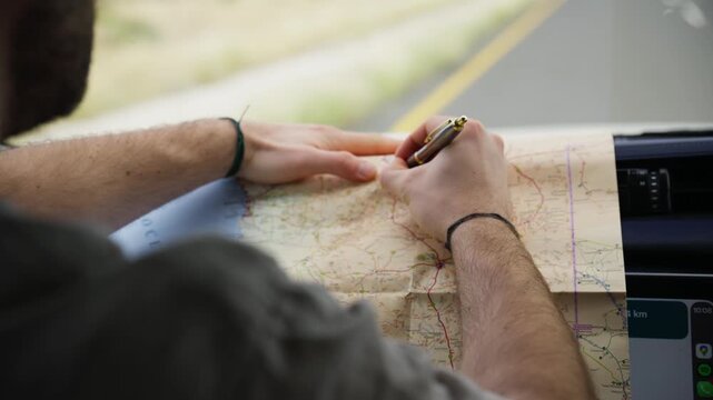 Adventurous traveler inside a moving car planning road trip journey and marking route on paper map of Namibia, highlighting destination with a pen