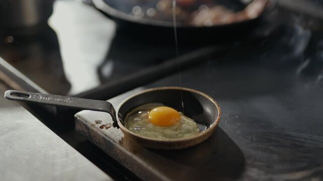 Hands crack egg into tiny pan. Yolk settles in warm, shallow skillet. Fingers show care, precision, and focus. Perfect for breakfast, cooking, or kitchen scenes. No animals, no plants