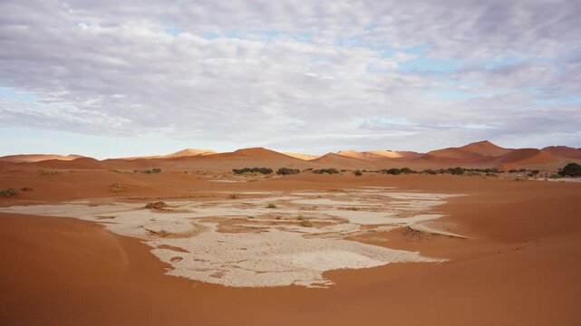 Scenic landscape of Deadvlei salt pan surrounded by red sand dunes in Namib Naukluft National Park, Namibia, with panning motion revealing immense scale of arid scenery