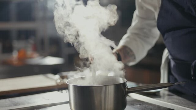 Steam rises from a pot as a chef stirs it. Hands show skill, focused, precise. Kitchen tools and steam create atmosphere. Professional cook works with care. Ideal for food, cooking