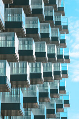 Modern architectural facade presenting a striking pattern of repeating glass balconies, creating an abstract and dynamic urban design with a bright blue sky backdrop © Newleks