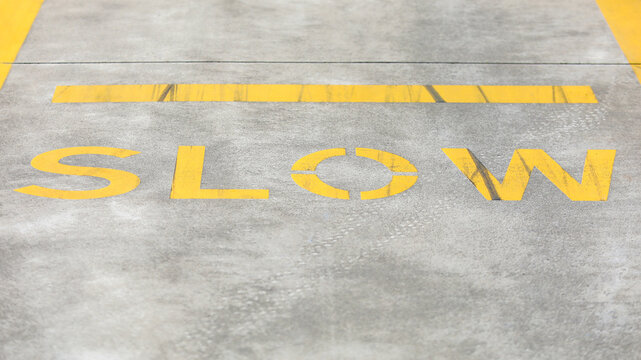 Yellow painted slow road marking on a grey asphalt road surface indicating a traffic warning to reduce vehicle speed and proceed with caution for safety