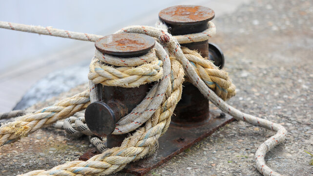 Rusty metal bollard securely holding thick mooring ropes on a concrete pier, representing marina infrastructure, naval safety, and strong maritime connections in port