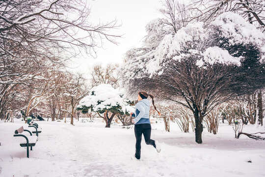 Back view of a woman jogging along a snowy path in a quiet winter park