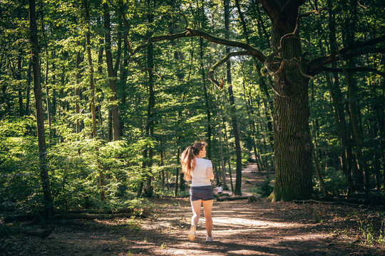 Young woman running along a forest trail in warm morning sunlight, enjoying nature and outdoor fitness