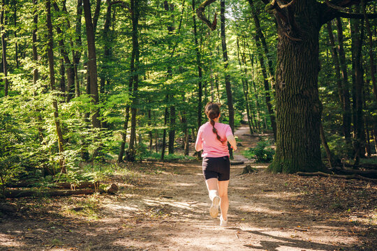 Active woman running through sunlit forest, enjoying peaceful and healthy lifestyle