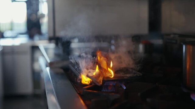 Hands flick a flame from a burner. Smoke curls above the hot pan. The cook's focus is sharp and precise. Flames dance as the chef stirs the mix. Culinary moment, intense and vivid