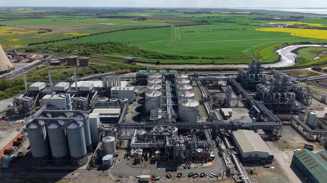 Aerial view of the Salt End industrial chemical park featuring storage tanks and complex piping systems surrounded by green fields and a river in Salt End, England, United Kingdom.