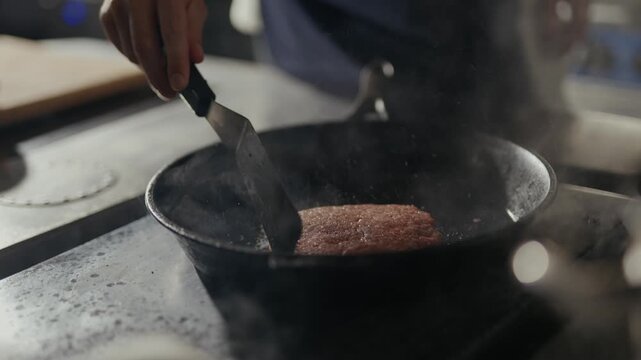 Chef flips sizzling steak in black skillet. Steam rises as meat cooks on hot surface. Kitchen tools and steam blur softly behind. Perfect for food, cooking, or restaurant scenes
