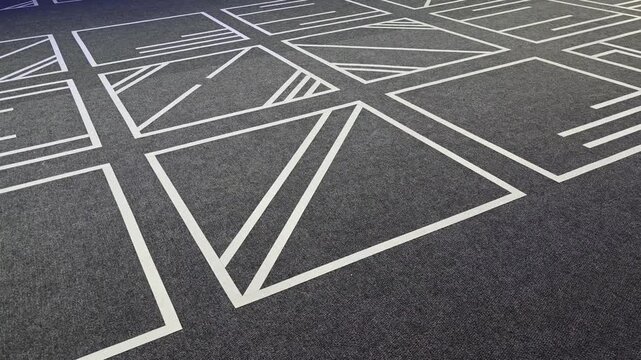 Dark gray carpet with a minimalist and modern design. White geometric lines creating a pattern of squares and triangles slowly revealing itself