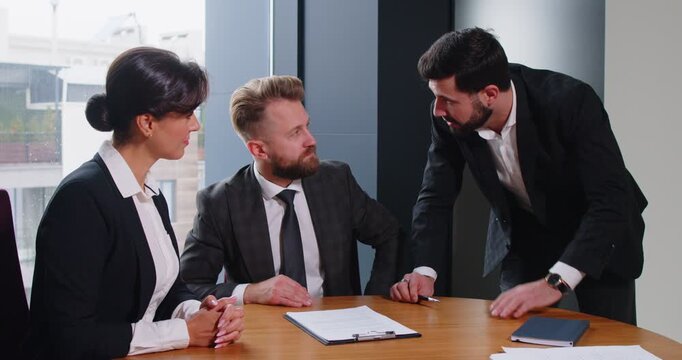 Three business professionals engaged in discussion about contract terms at office desk. Agent and clients reviewing details, exchanging opinions and making important decision before signing agreement.