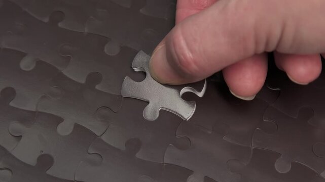 Human hand placing final piece to complete black jigsaw puzzle close-up, solution to assigned tasks, achieving success