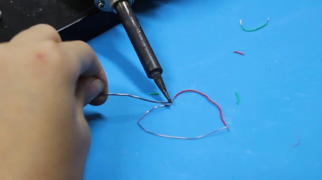 An unrecognizable boy is splicing two wires to build a robot inside an educational club in Neiva, Huila, Colombia. Concept of electricity and handmade
