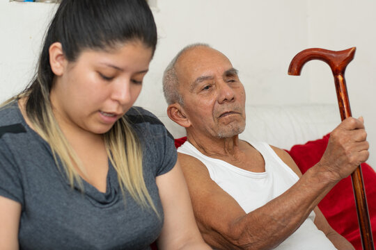 Elderly man holding cane while granddaughter assists him during daily home routine