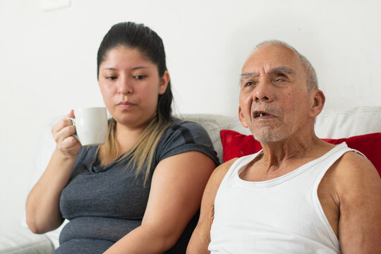 Young woman holding coffee while elderly grandfather sits beside her in shared home moment