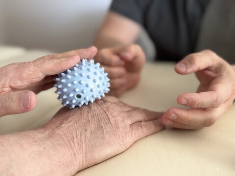 Close-up of elderly person doing hand rehabilitation with therapist using a massage ball. Concept of physiotherapy, recovery, healthcare, aging population, and assisted care.