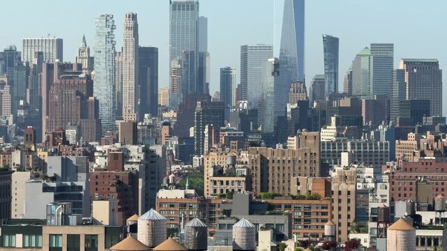 Dense New York City skyline with historic rooftops, wooden water towers, and modern skyscrapers. Urban architecture and residential buildings create a layered metropolitan cityscape under clear