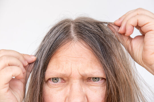 Mature woman touching her gray hair, examines silver strands, deep in thought, aging process, menopause time, emotional reflection, quiet acceptance
