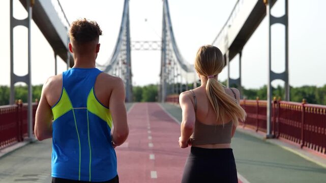 Young man and woman in sportswear doing sports, running on the bridge in the morning. Back view. Healthy lifestyle. Sport concept. Real time