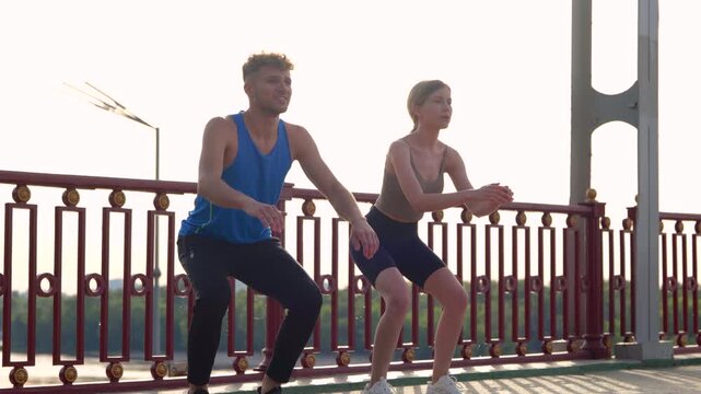 Smiling couple warming up while crouching before jogging, standing on the bridge. River on the background. Fitness, sport, lifestyle concept. Real time