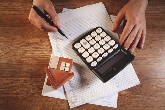 Businessman working at office desk with calculator and house model. Top view
