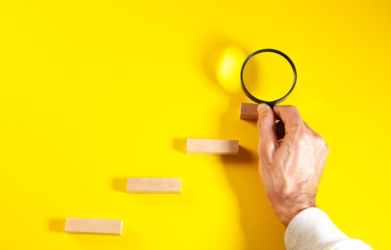 Top view of man's hand holding magnifying glass and wooden block on yellow background