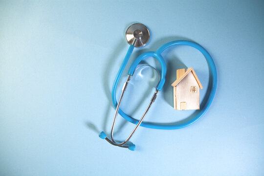 blue medical stethoscope and a house in the form of a heart on a wooden background,