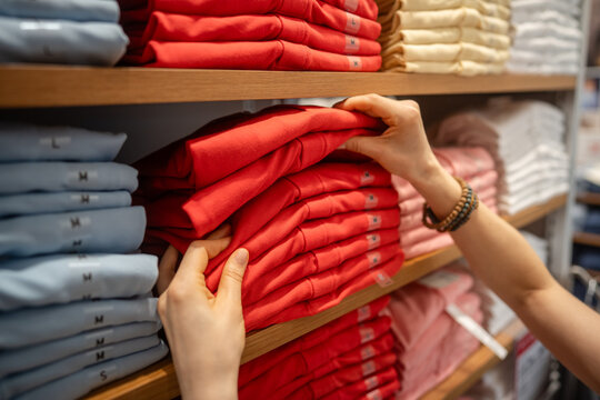 Woman buyer shopping for outfit in fashion selective shop, choosing apparel from shelf display, female customer searching for size and checking garment quality and content of fabric at retail store.