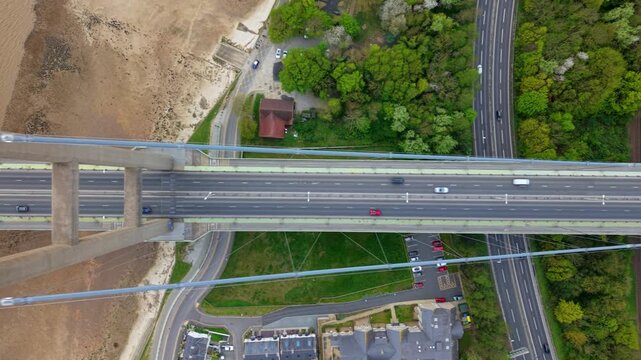 Aerial view of the Humber Bridge with cars driving across the suspension span above roads and green woodland in Hessle, East Riding of Yorkshire, United Kingdom.