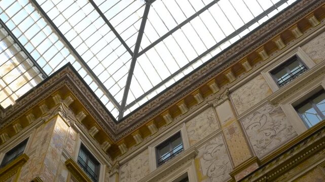 Ornate building interior rotating up towards glass ceiling. Low-angle view rotating toward a magnificent glass ceiling in a historic building, highlighting ornate frescoes