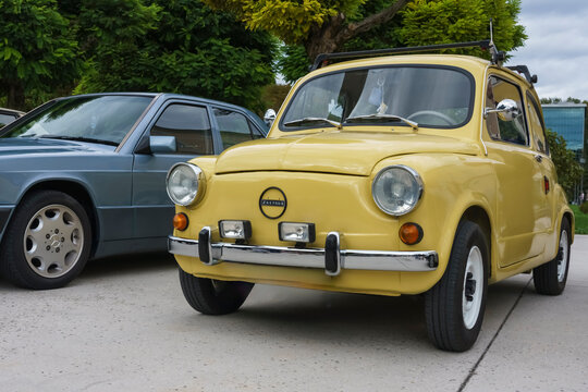 Rogaska Slatina, Slovenia. Vintage yellow Zastava car parked beside a blue sedan on a concrete surface with greenery in the background