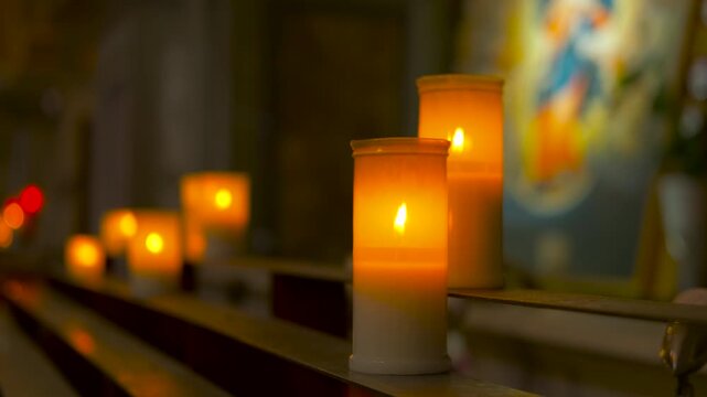 Row of burning prayer candles in a church. Flickering flames of prayer candles arranged in a row inside a dark, serene church, casting a warm and spiritual glow with a blurred icon in the background