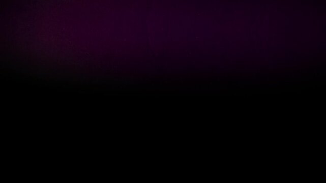 Abstract purple and pink light leak flickering at the top of a dark black background with subtle paper texture and grain. Concept of artistic lighting and elegant overlay