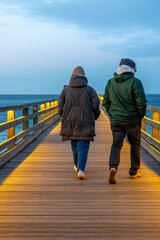 Fototapeta premium Couple walking on wooden pier. Evening stroll by the sea.