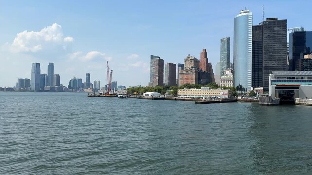 Expansive harbor perspective showing Manhattan skyscrapers and waterfront buildings under bright sky. Peaceful urban panorama represents travel, tourism, and modern city life in the United States.