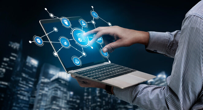 A person interacts with a futuristic digital interface on a laptop, symbolizing advanced technology and connectivity in a cityscape backdrop at night. Tessel