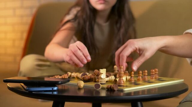 Mother and daughter preparing chess board for a game. Woman and a young girl placing wooden chess pieces on the board before starting a family game, spending quality time together at home
