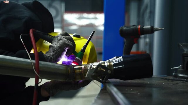 4k video Worker performs TIG welding on metal using a tungsten electrode with argon shielding gas, wearing a protective welding helmet for safety.